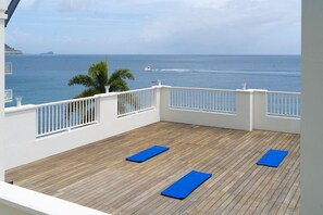 Una terraza de madera con alfombras azules, barandillas blancas y vista al océano.