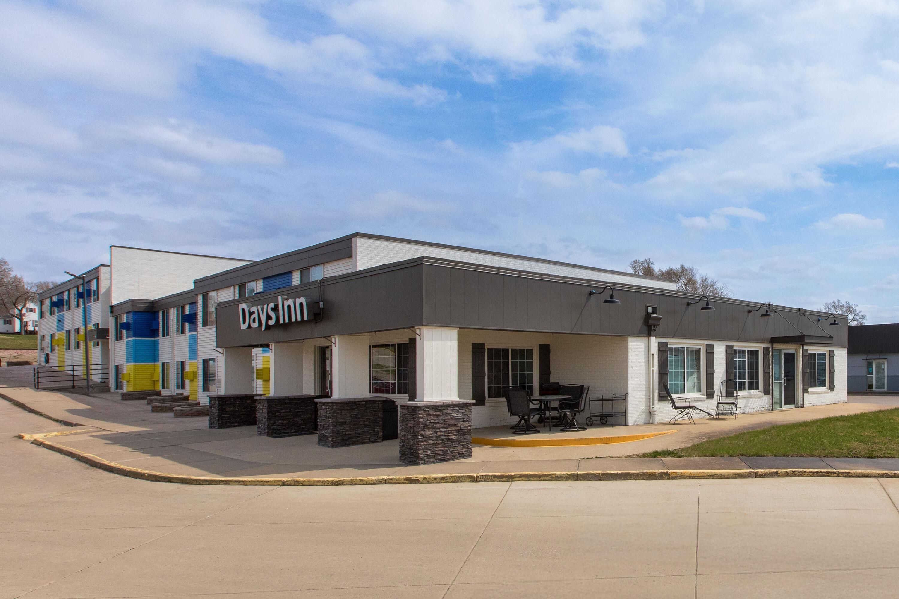 A Days Inn with a modern exterior, outdoor seating area, and a clear sky.