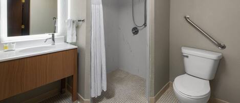 A bathroom with a white sink, mirror, and toilet. There is a shower with a handheld showerhead and a grab bar. The floor is tiled.