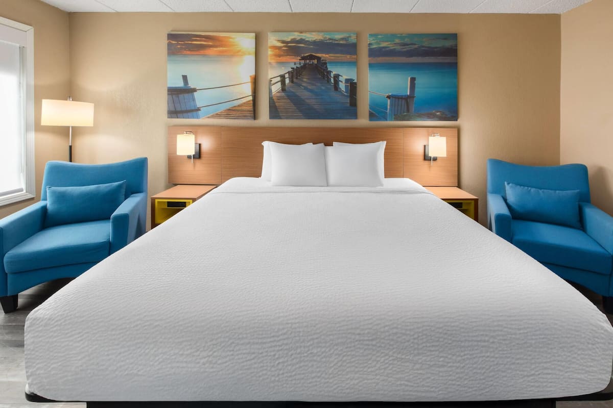 Habitación de hotel con una cama grande, dos sillones azules, un cabecero de madera y tres lámparas fijadas a la pared.