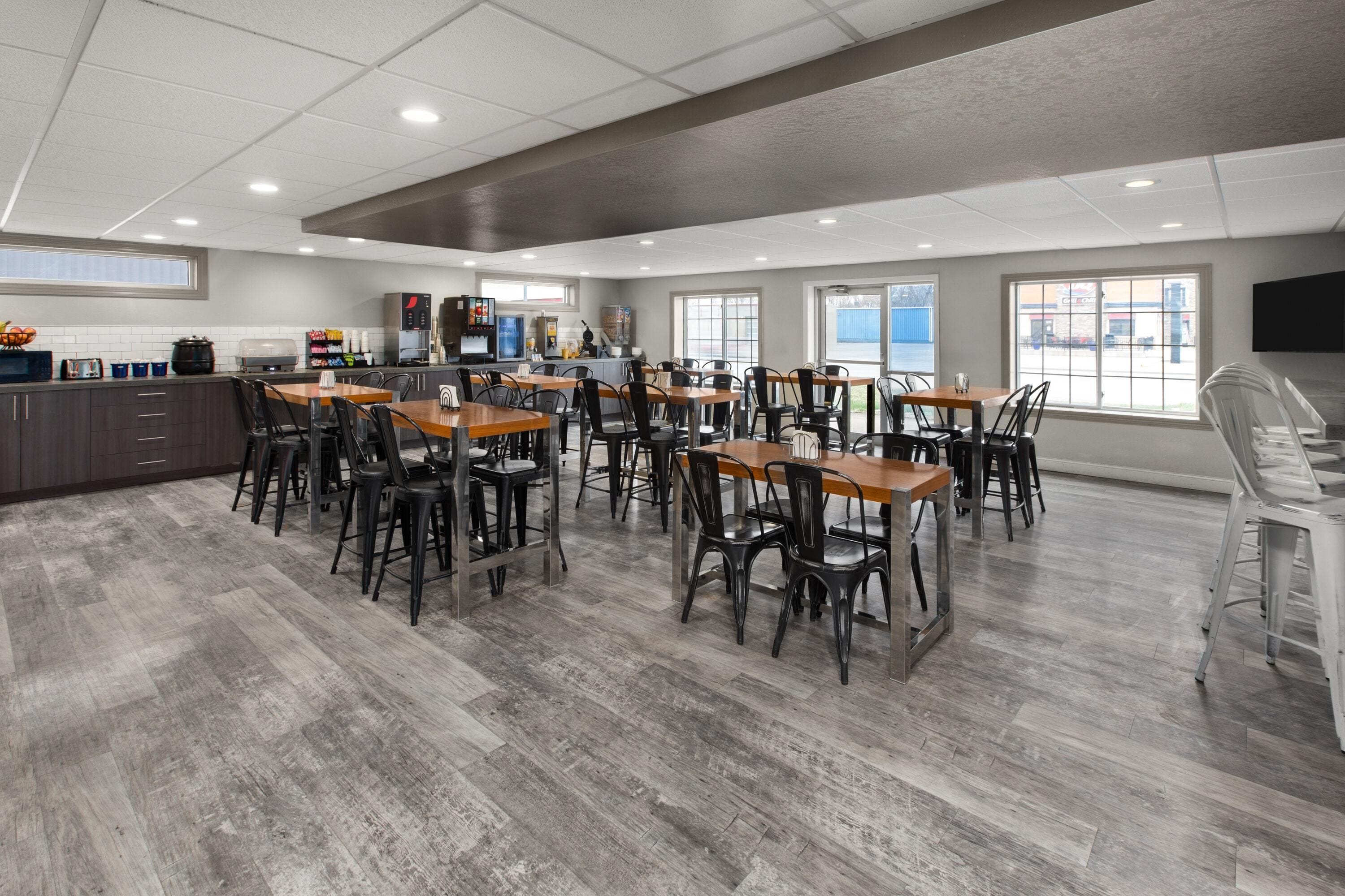 A spacious dining area with multiple tables and chairs, a kitchen area with appliances, and large windows providing natural light.