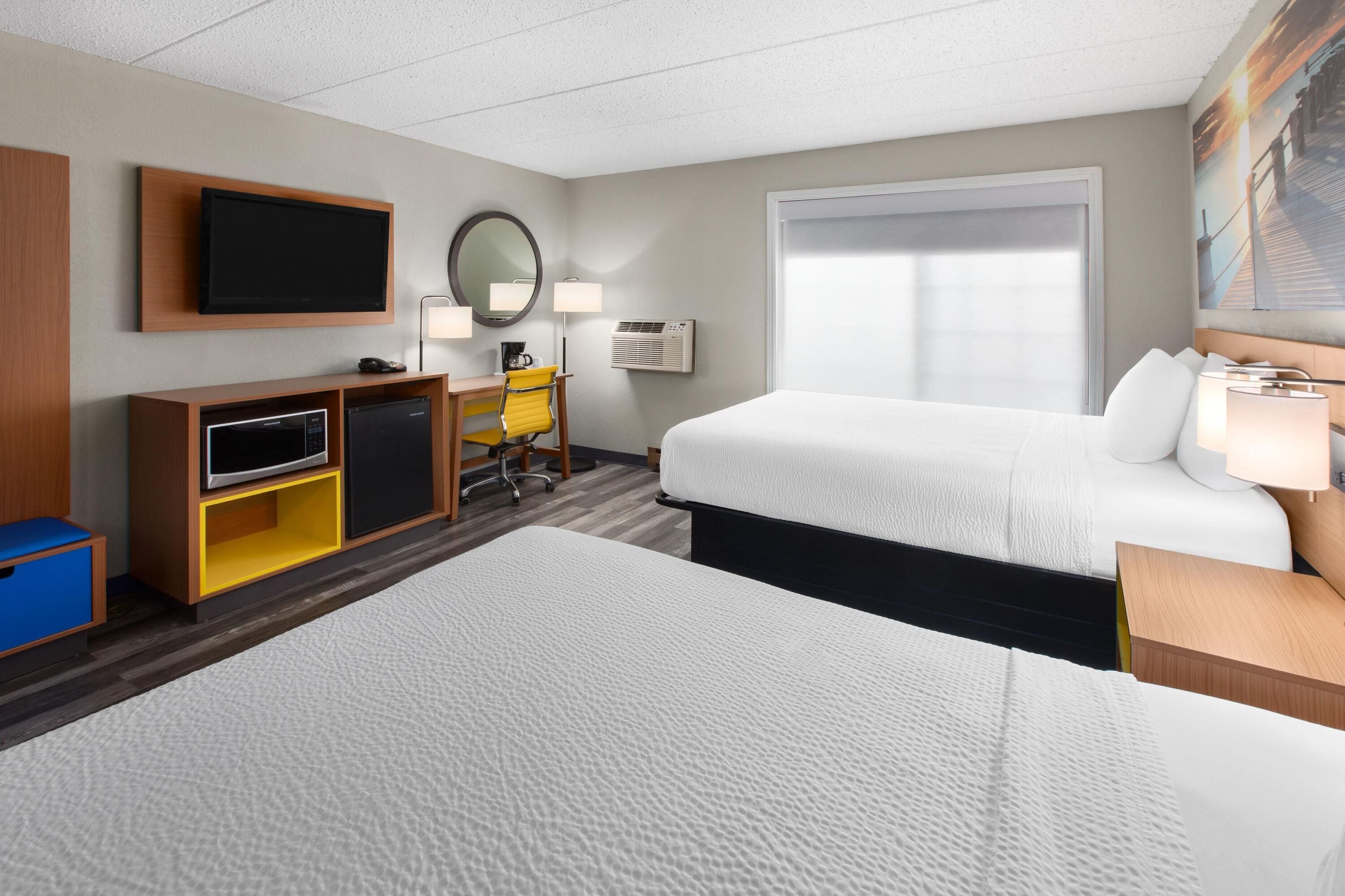 Une chambre d’hôtel avec deux lits, un bureau avec une chaise, une télévision et une grande fenêtre.