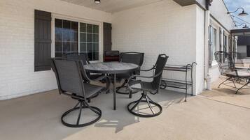 An outdoor patio with a round table and four chairs, a grill, and a white brick wall.