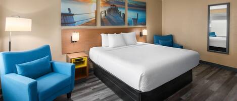 Hotelkamer met een groot bed, twee blauwe fauteuils, een houten hoofdbord, een nachtkastje, een lamp en drie aan de muur bevestigde schilderijen.