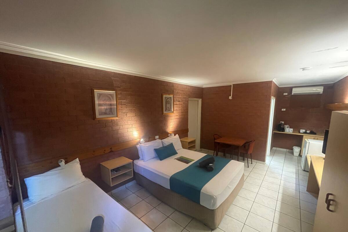 Una habitación de hotel con dos camas, un escritorio pequeño, una silla, una kitchenette y un baño.