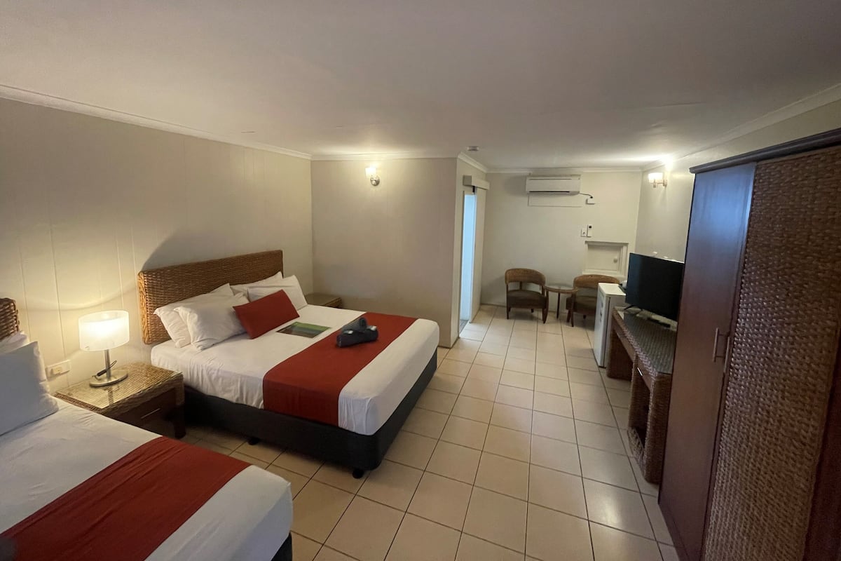 Habitación de hotel con dos camas, un escritorio, una silla, un televisor y un equipo de aire acondicionado.