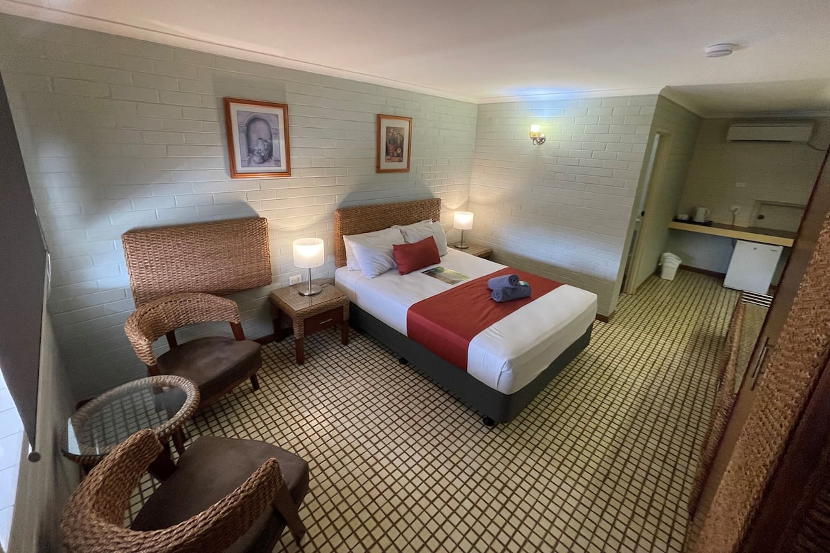 Una habitación de hotel con una cama, dos mesitas de noche, una silla, una pequeña mesa y una kitchenette.