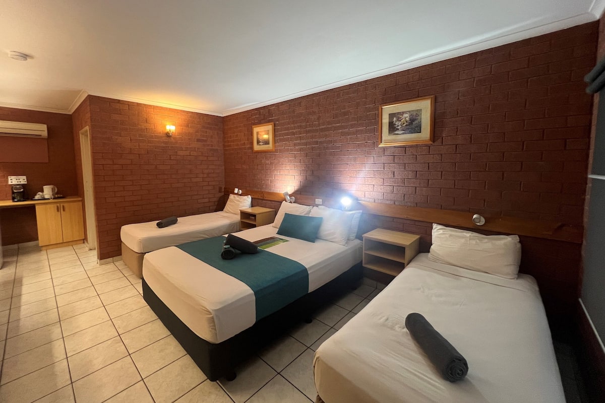 Habitación de hotel con dos camas, una kitchenette pequeña y una pared de ladrillo.
