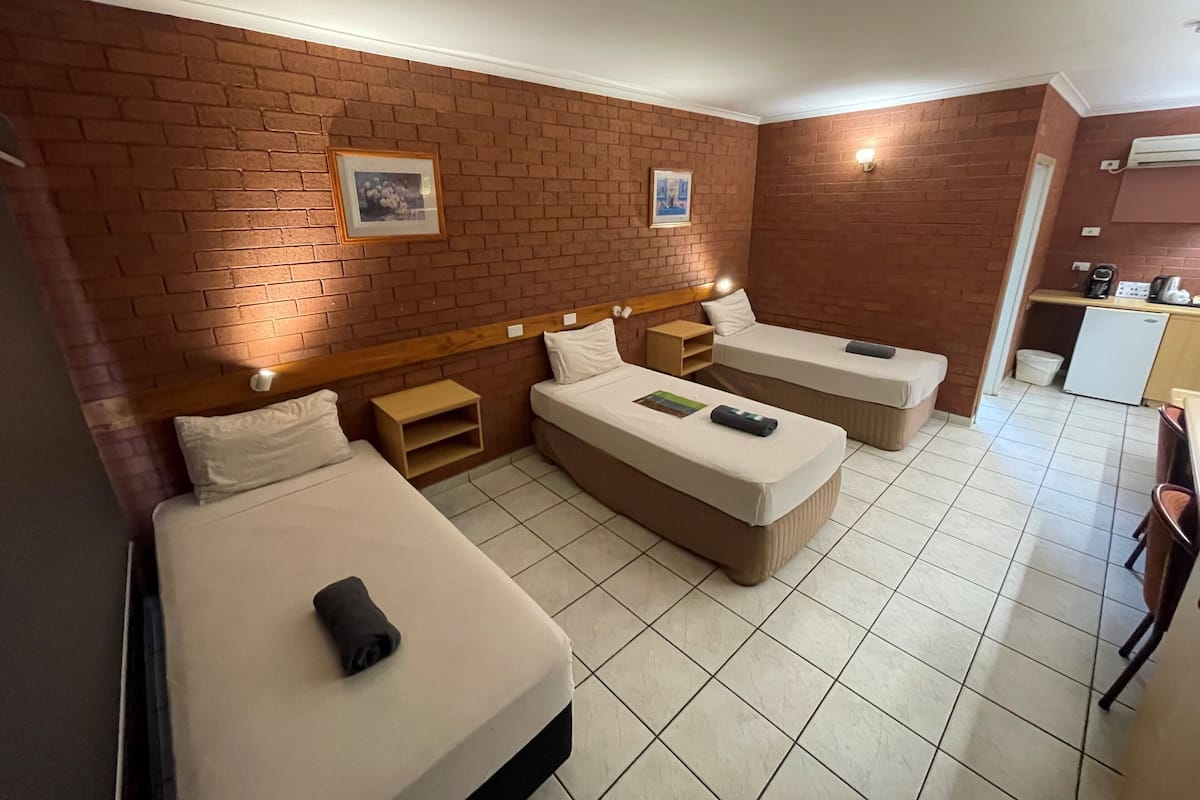 Una habitación de hotel con tres camas, una mesita de noche de madera, un refrigerador y una cafetera.