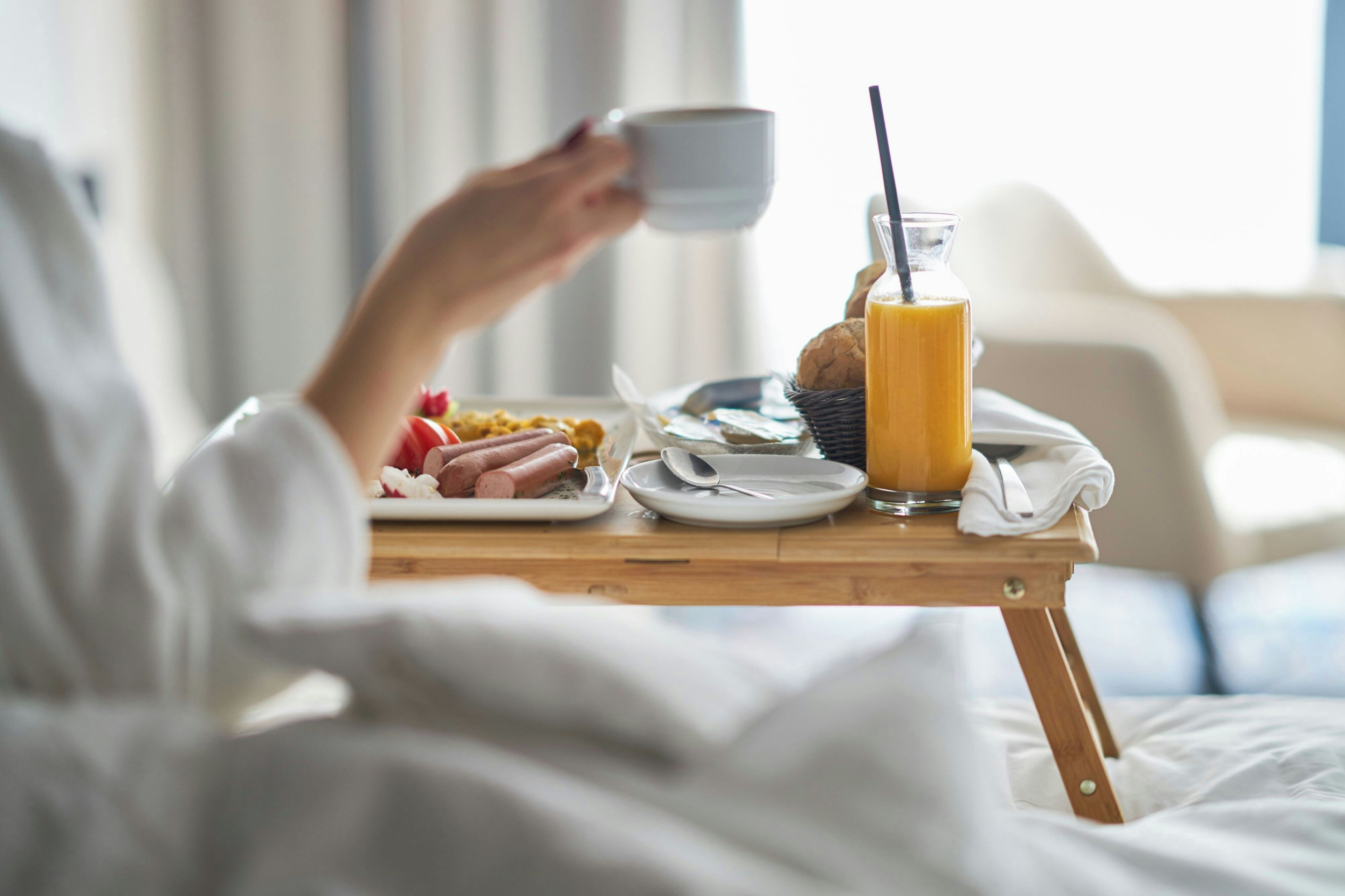 Un desayuno con una taza, un vaso de zumo de naranja y un plato de comida que incluye salchichas y un muffin.