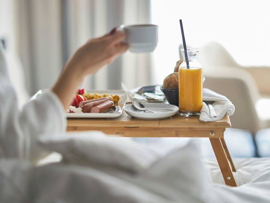 Un desayuno con una taza, un vaso de zumo de naranja y un plato de comida que incluye salchichas y un muffin.
