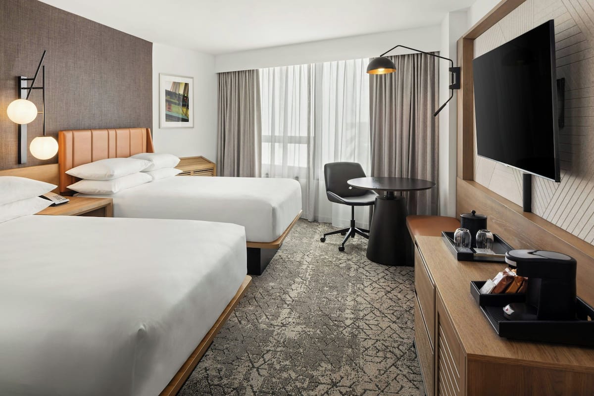 A hotel room with two beds, a desk, a chair, a TV, and a coffee machine.