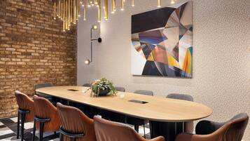 A conference room with a long table, brown leather chairs, a potted plant, and a modern abstract painting on the wall.