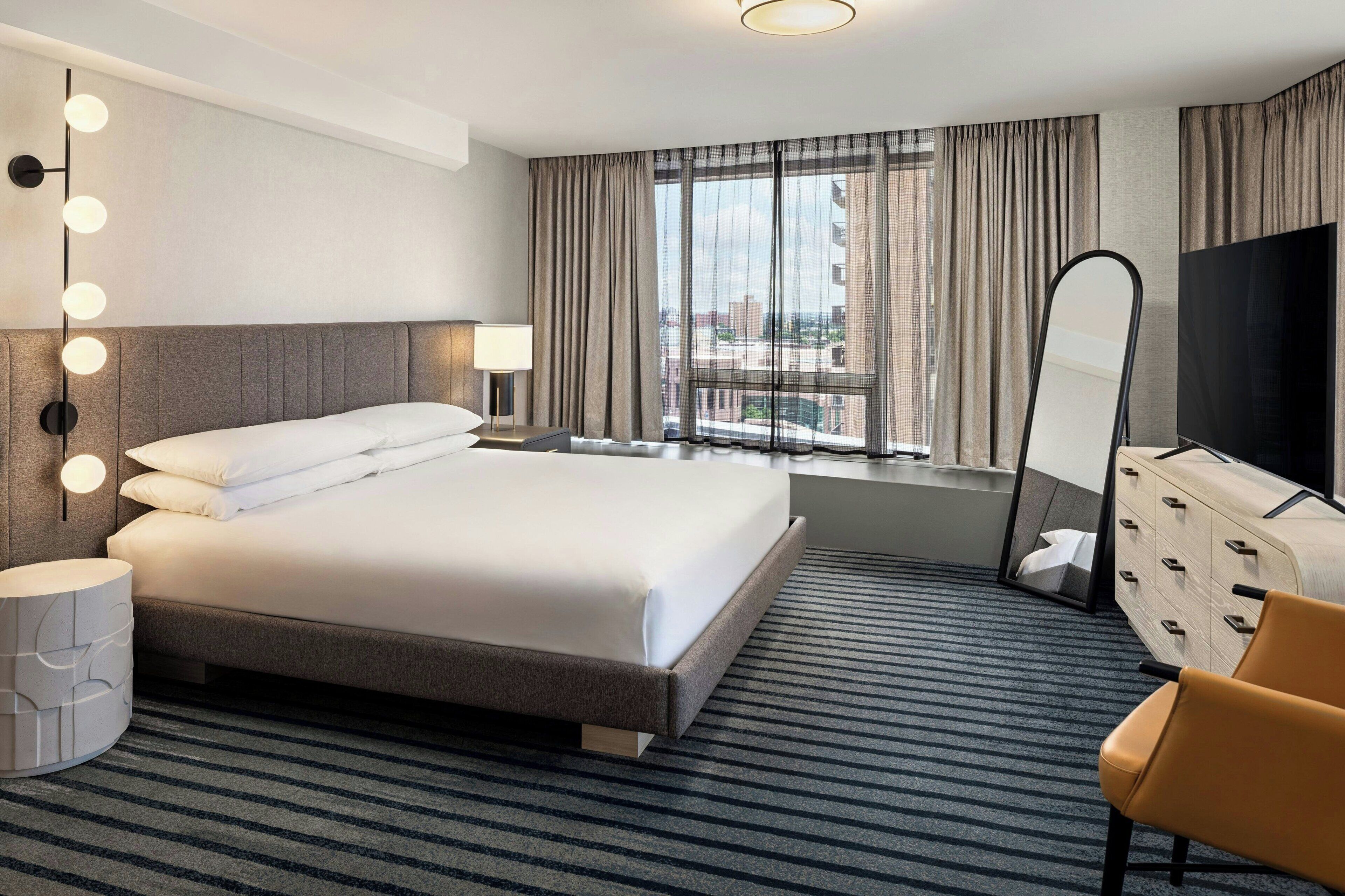 Une chambre d’hôtel avec un grand lit, une télévision, un miroir et une fenêtre avec des rideaux.