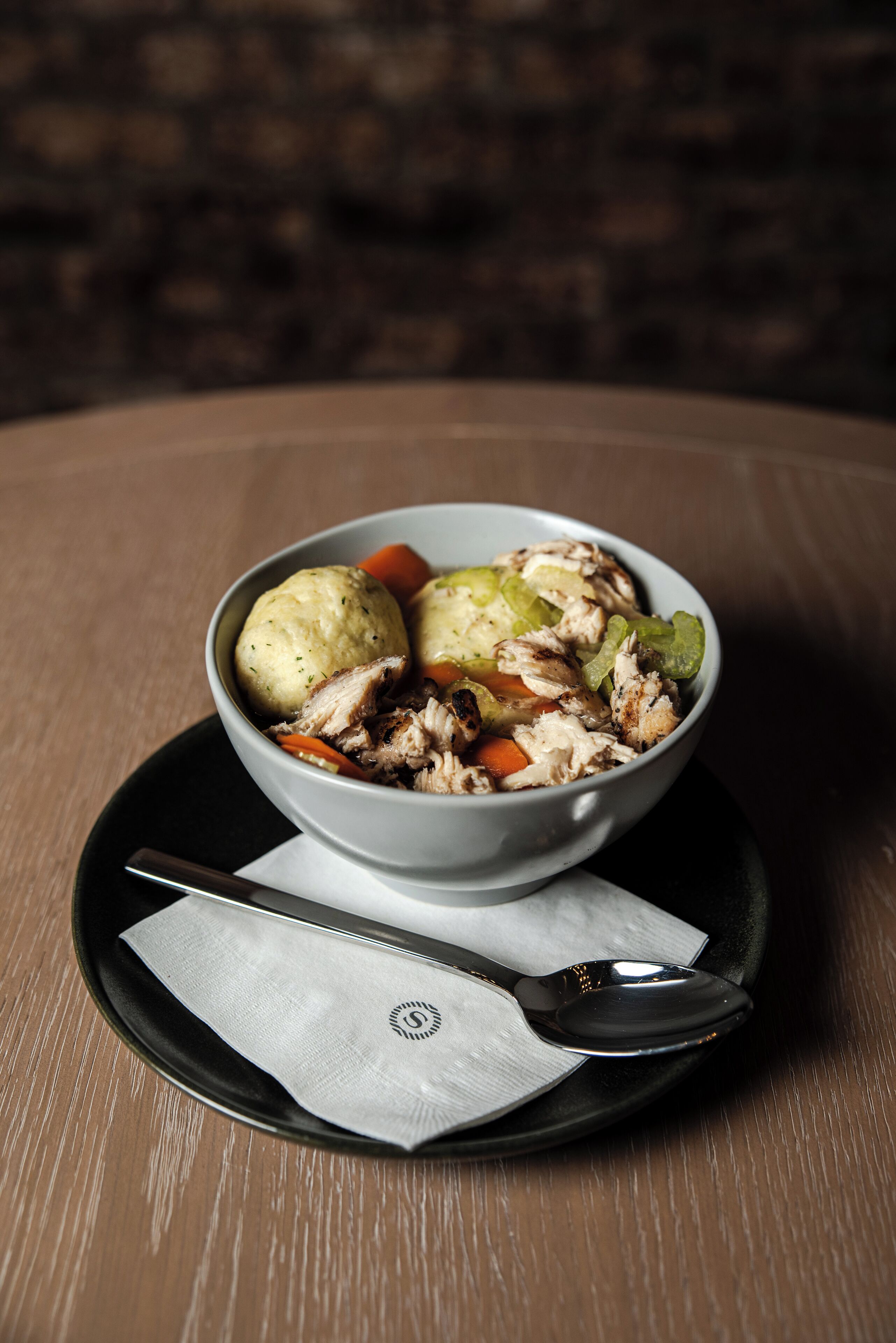 A bowl of food on a table with a napkin and spoon beside it.