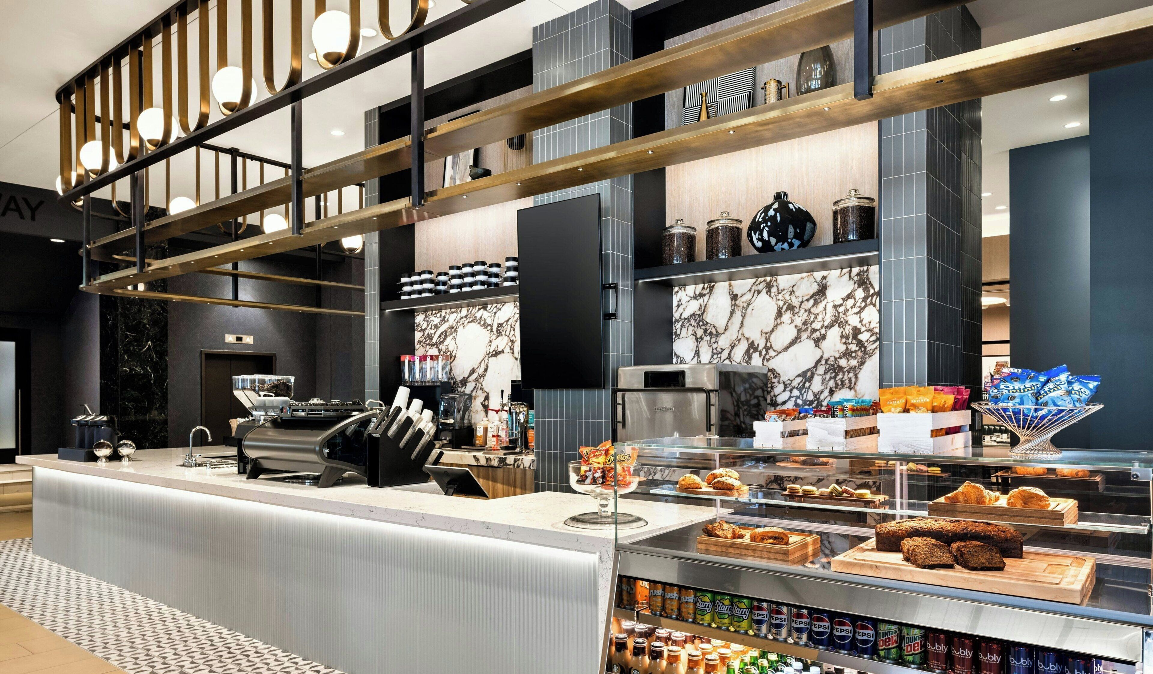 Una cafetería moderna con salpicadero de mármol, máquina de espresso, pastelería y diversas bebidas.