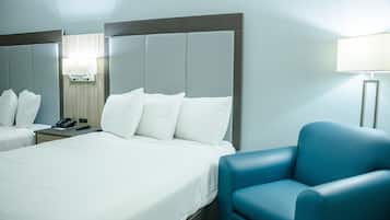 Una habitación de hotel con dos camas, un sillón azul, una mesita de noche con un teléfono y una lámpara.