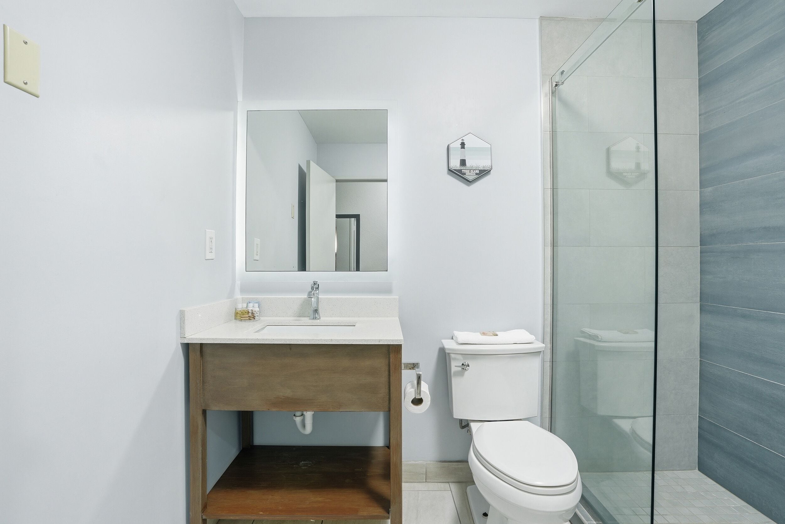 A modern bathroom with a wooden vanity, a white sink, a toilet, and a glass shower enclosure.