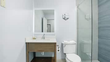 Un baño moderno con tocador de madera, un lavamanos blanco, un inodoro y una cabina de ducha de vidrio.