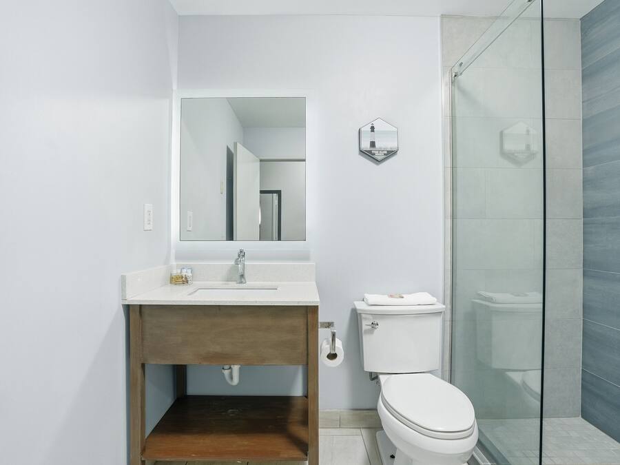 Un baño moderno con tocador de madera, un lavamanos blanco, un inodoro y una cabina de ducha de vidrio.