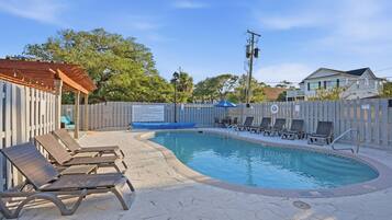 A swimming pool with lounge chairs, a pergola, and a fenced area with a sign.