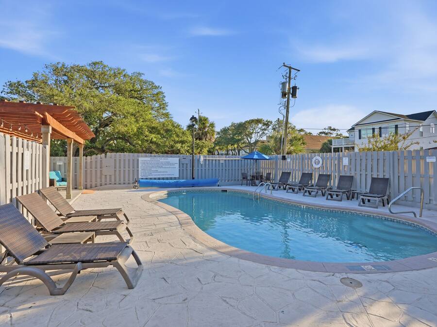 A swimming pool with lounge chairs, a pergola, and a fenced area with a sign.