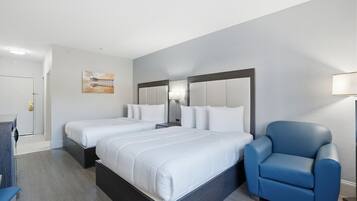 A hotel room with two beds, a blue armchair, a desk, and a painting on the wall.