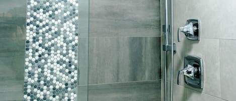 A shower with a glass partition and a tiled wall.