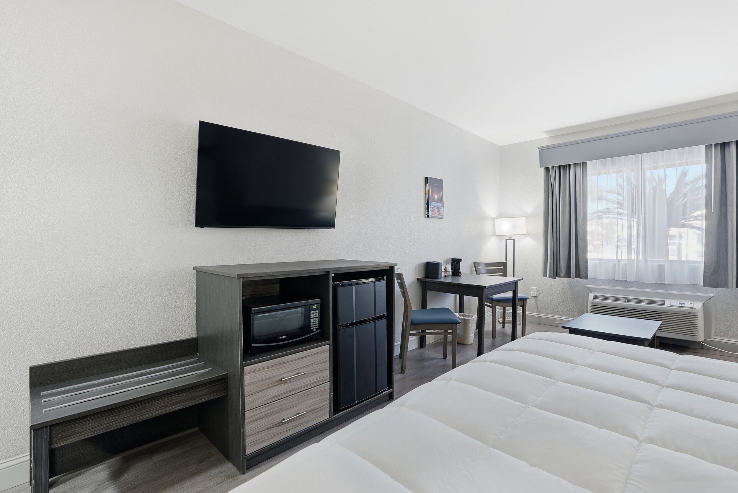 Ein Hotelzimmer mit Bett, Schreibtisch mit Computer, Fernseher und einem Fenster mit Vorhängen.