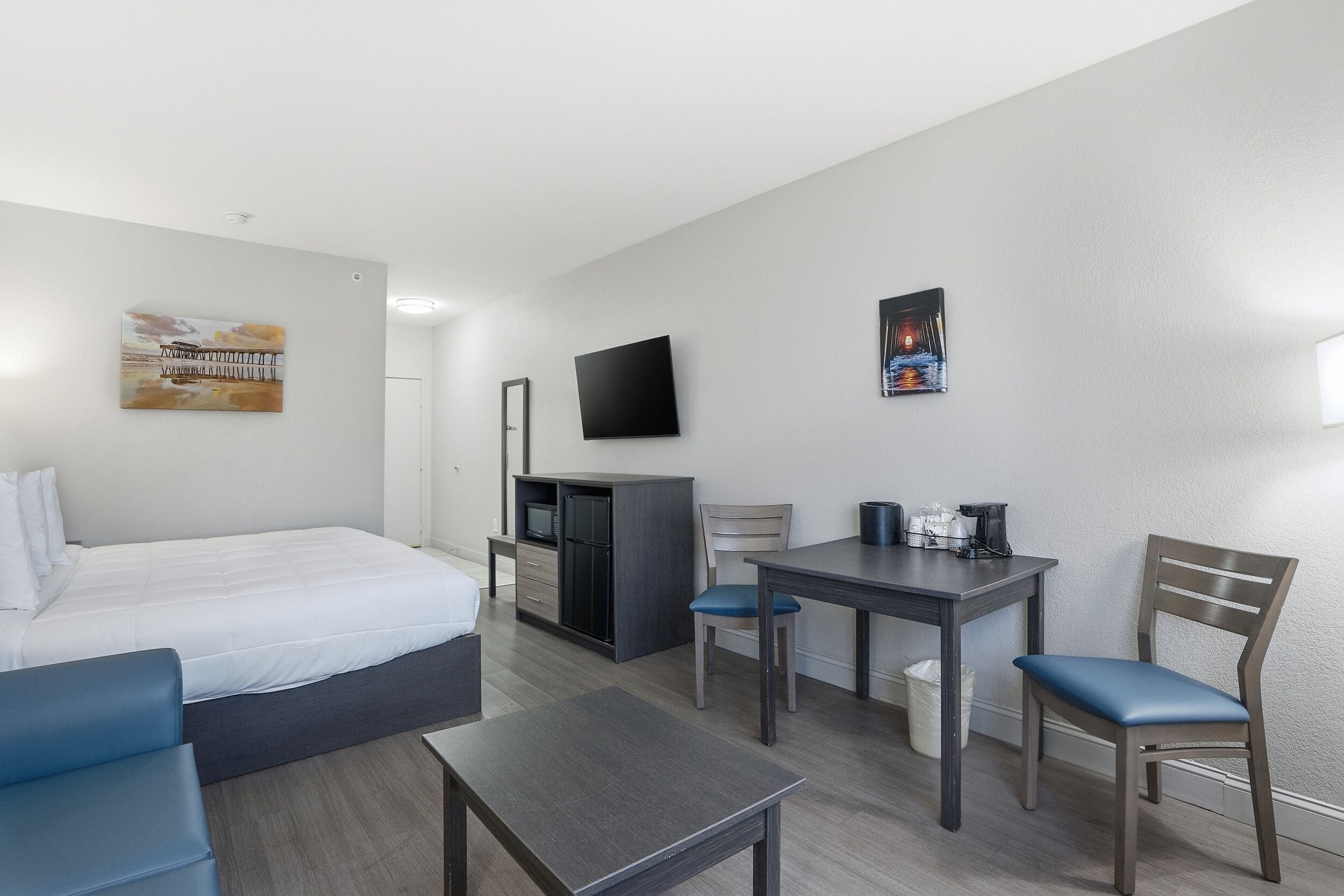 Ein Hotelzimmer mit einem Bett, einem Schreibtisch, einem Sessel, einem Fernseher und Kunstwerken an den Wänden.