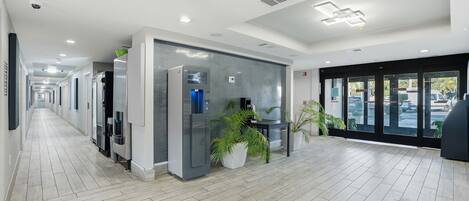 A hotel lobby with a long corridor, an exit sign, a water dispenser, and potted plants.