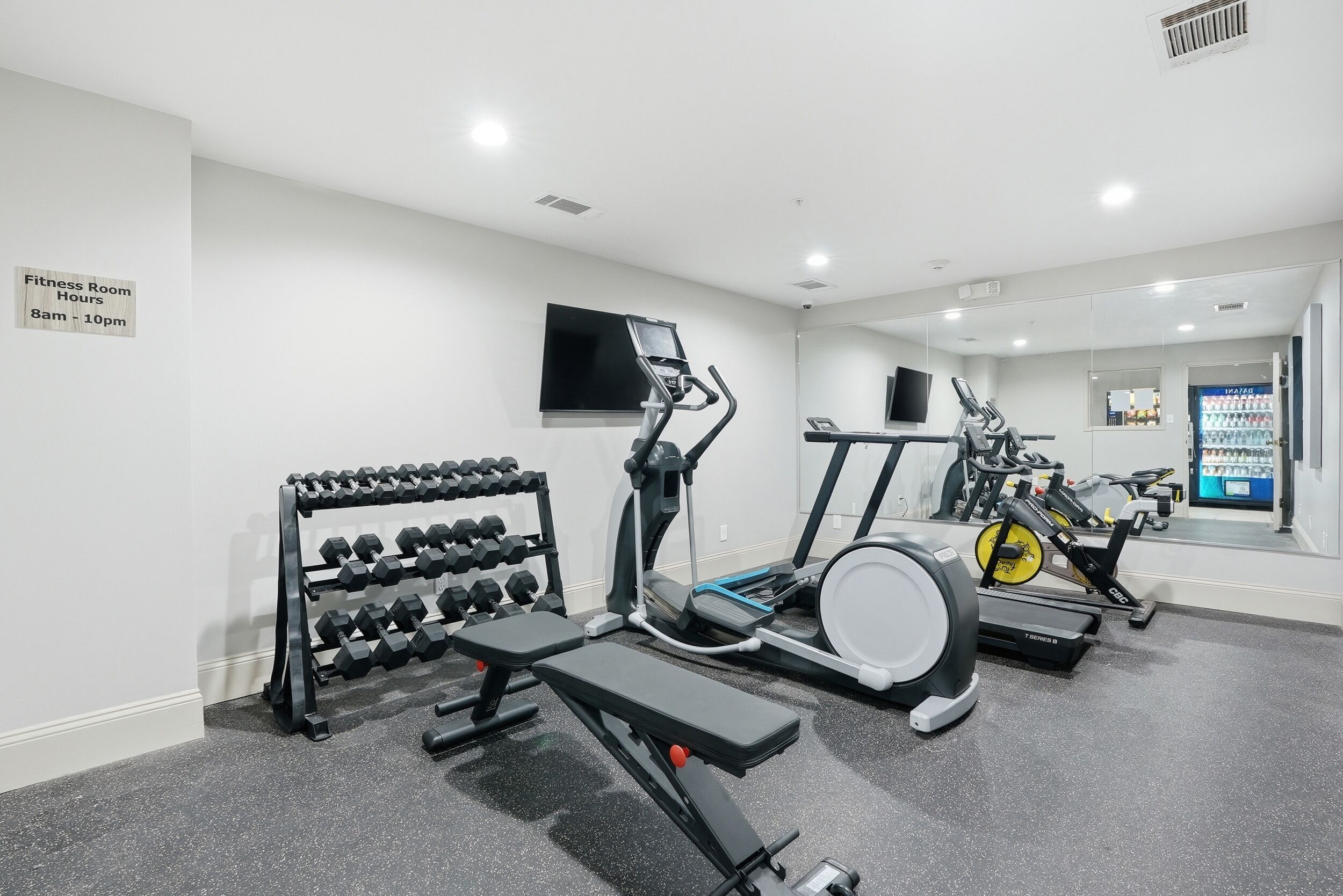 A fitness room with dumbbells, a bench, and cardio equipment.