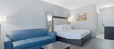 A hotel room with a blue sofa, a bed with white bedding, a small table, and a painting on the wall.