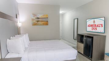 Ett hotellrum med en säng, ett skrivbord, en stol, en tv och en tavla på väggen.