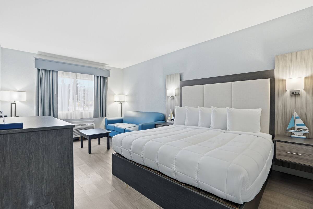 A hotel room with a large bed, a desk, a blue sofa, and a small table.