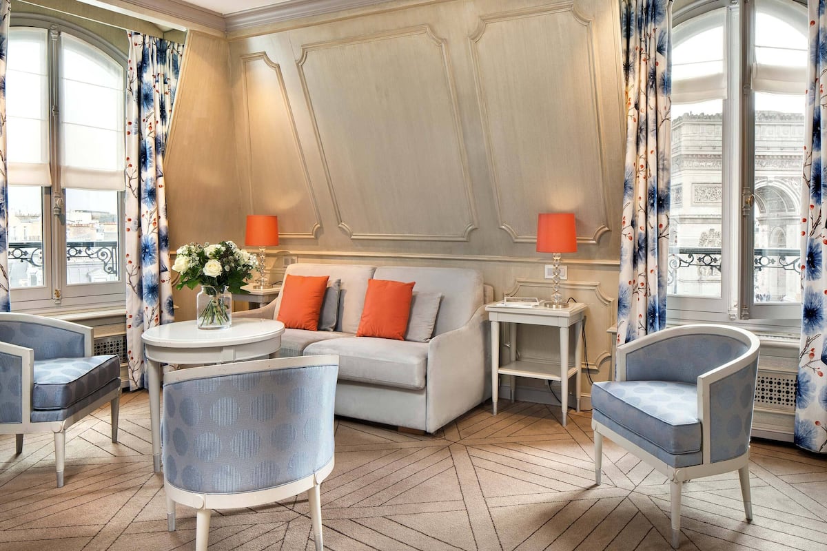 A room with a sofa, two armchairs, a small table, and two lamps.