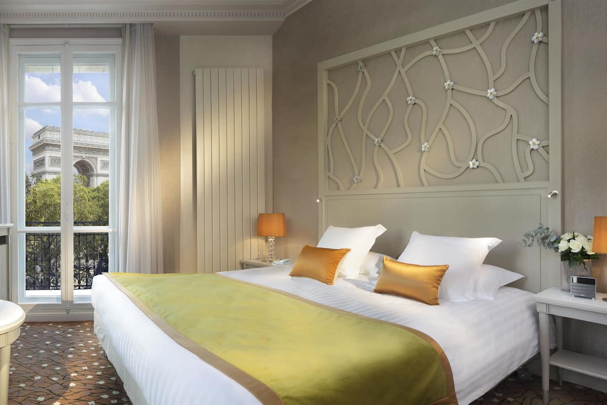A hotel room with a large bed, a television, a small table with a vase of flowers, and a view of the Eiffel Tower through the window.