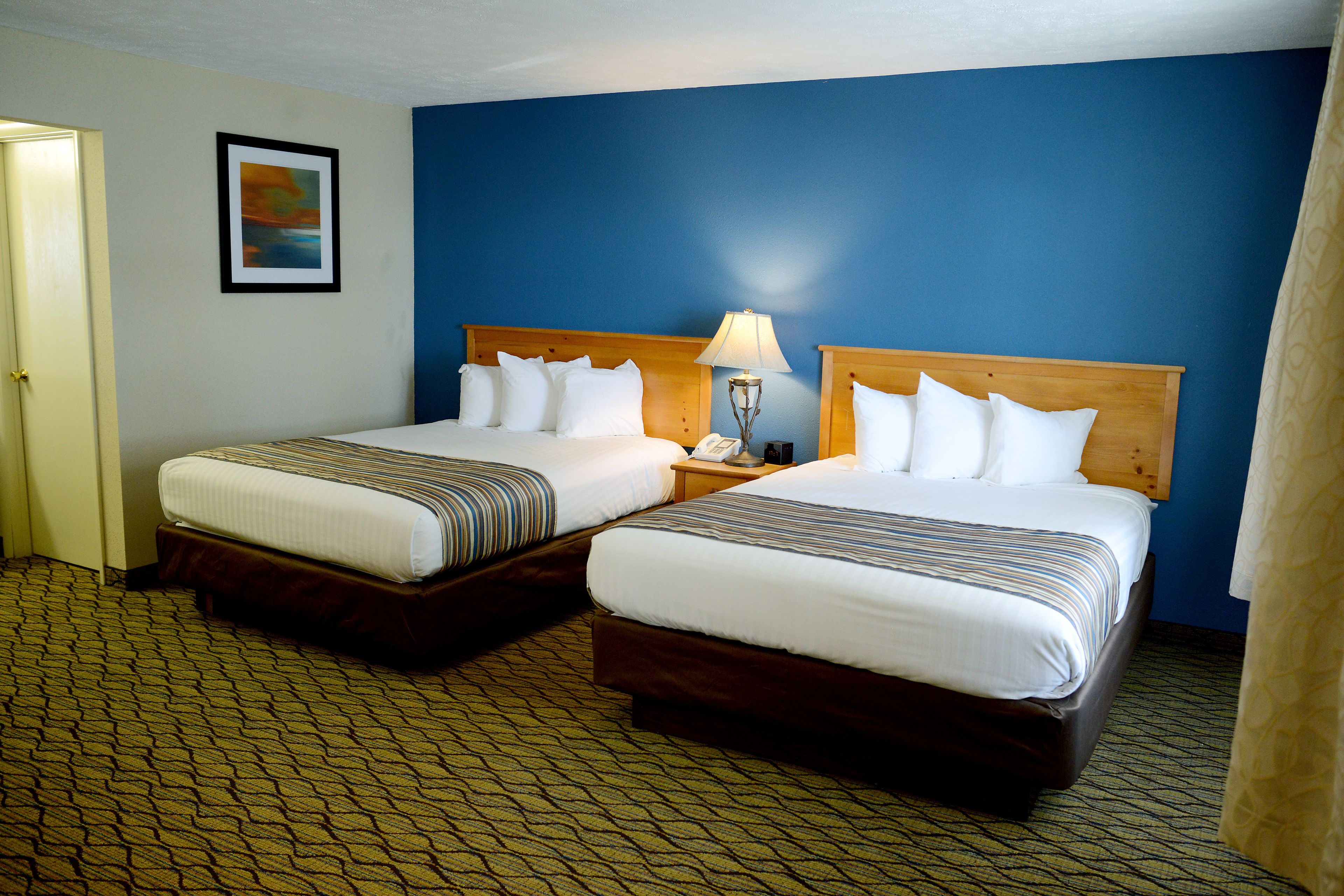A hotel room with two beds, a nightstand with a lamp, and a painting on the wall.