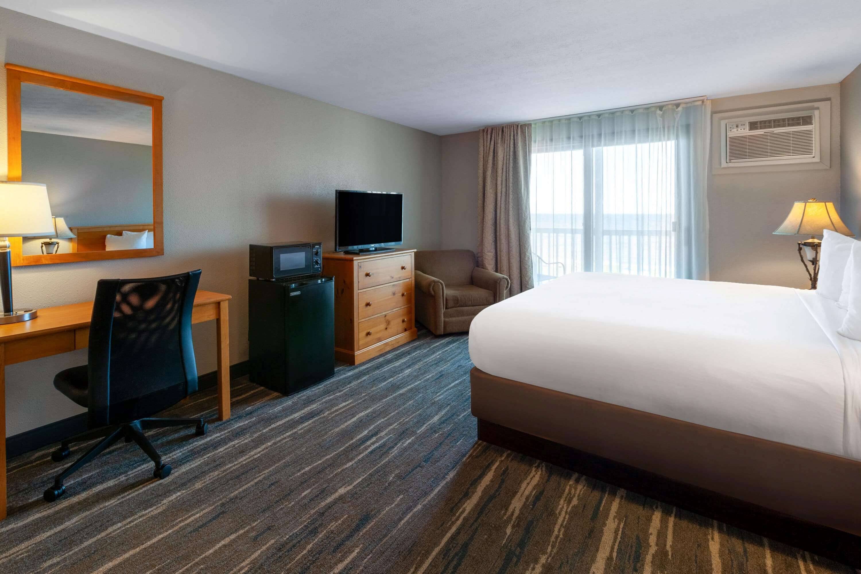 Habitación de hotel con cama, escritorio con computadora, televisor, silla y cómoda.