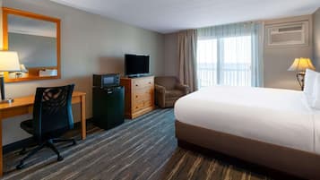 Habitación de hotel con cama, escritorio con computadora, televisor, silla y cómoda.
