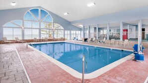 An indoor swimming pool with clear blue water, surrounded by lounge chairs and a tiled floor.