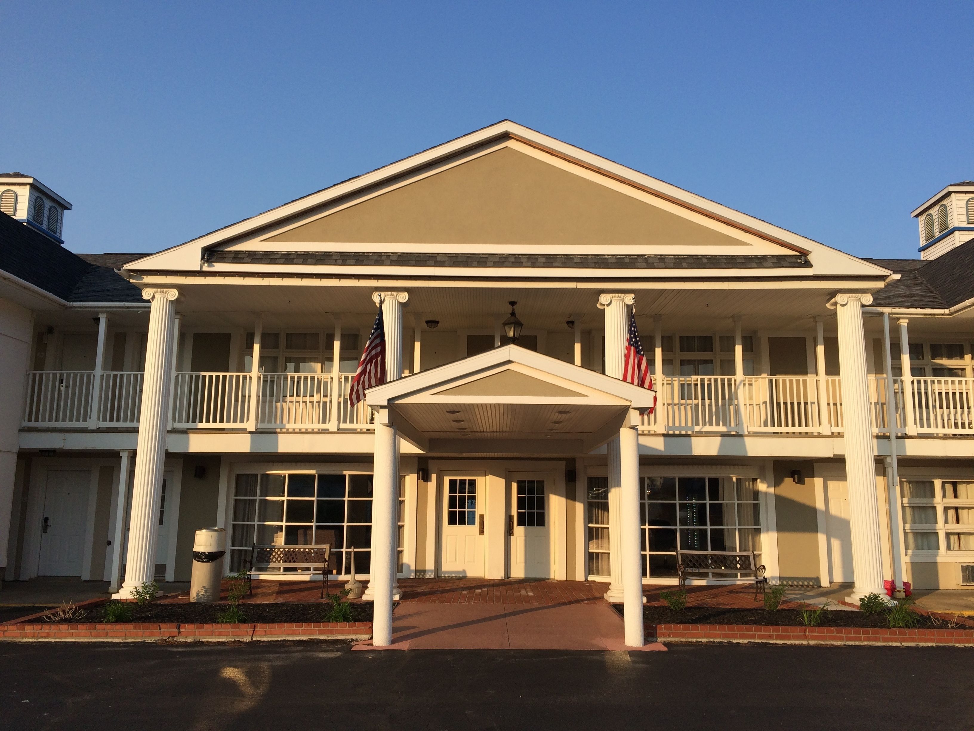 A two-story building with a central entrance, columns, and a balcony with railings.