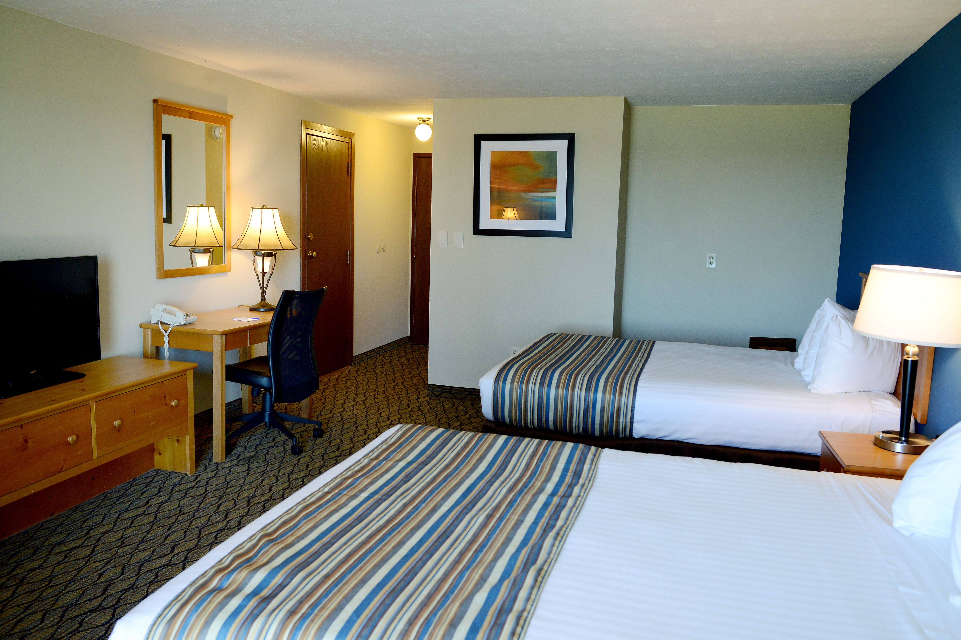 A hotel room with two beds, a desk with a chair, a television, and a painting on the wall.