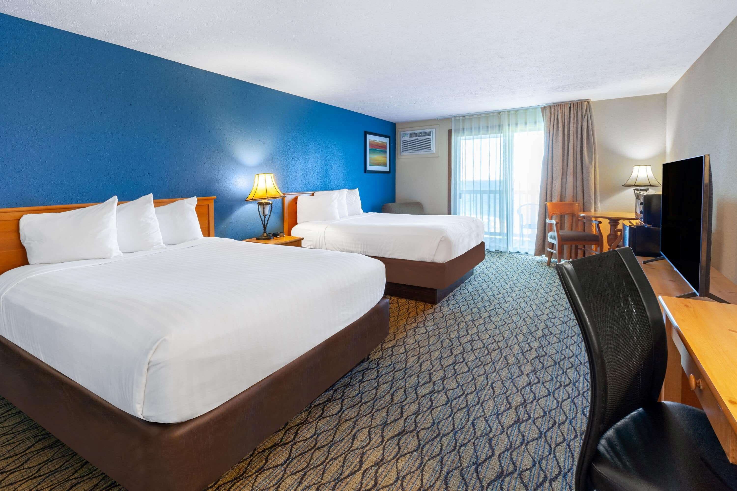 Une chambre d’hôtel avec deux lits, un bureau, une chaise, une télévision et une fenêtre avec des rideaux.