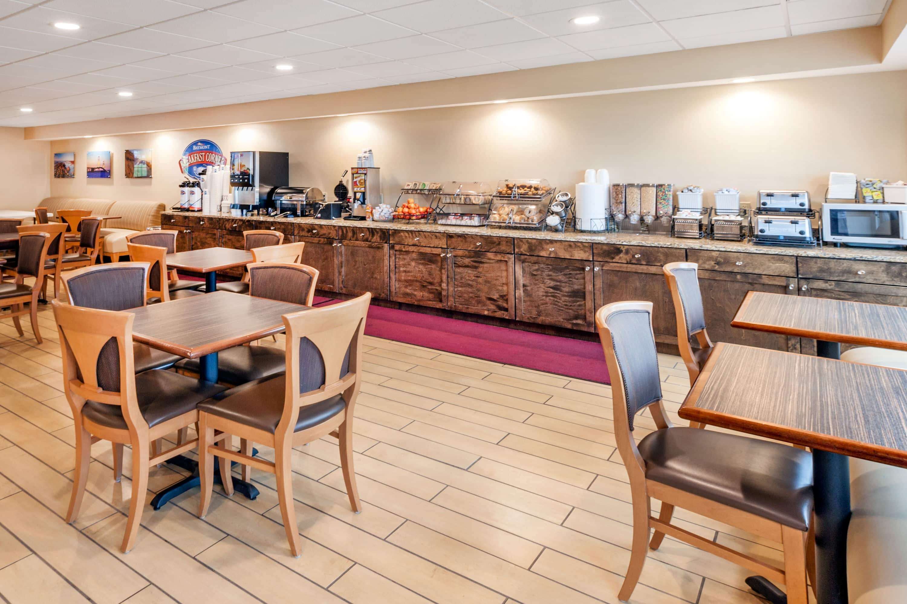 Un espace réservé au petit-déjeuner, avec des tables et des chaises en bois, un coin café et une variété d’aliments.