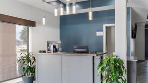 Un espace d’accueil avec un comptoir, une machine à café et deux plantes en pot.