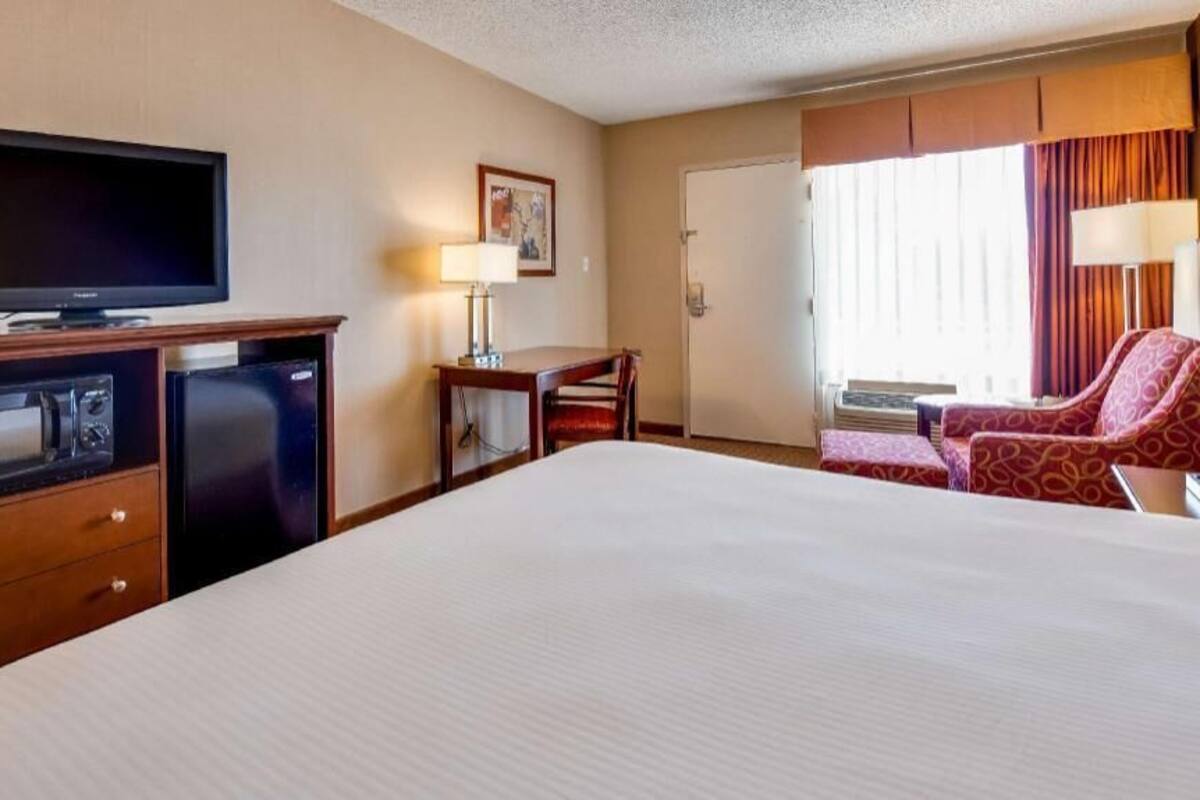 A hotel room with a bed, a television, a desk, a chair, and a window with curtains.