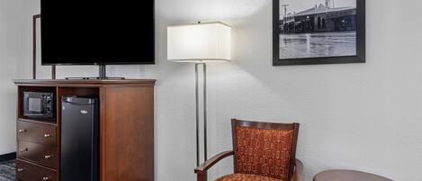Une chambre d’hôtel équipée d’une télévision à écran plat, d’un bureau avec un micro-ondes, d’un réfrigérateur, d’une chaise, d’une lampe et d’un tableau encadré au mur.