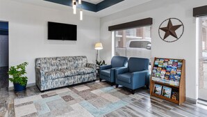 Un hall d’entrée avec un canapé à motifs, deux fauteuils, un présentoir à magazines et une décoration en forme d’étoile sur le mur.