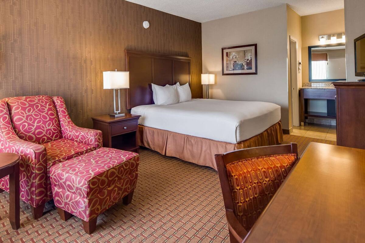 A hotel room with a bed, a chair, a desk, and a lamp.